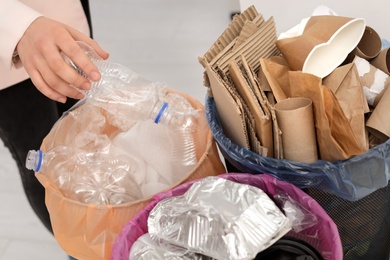 Photo of Woman putting used plastic bottle into trash bin, closeup. Waste recycling