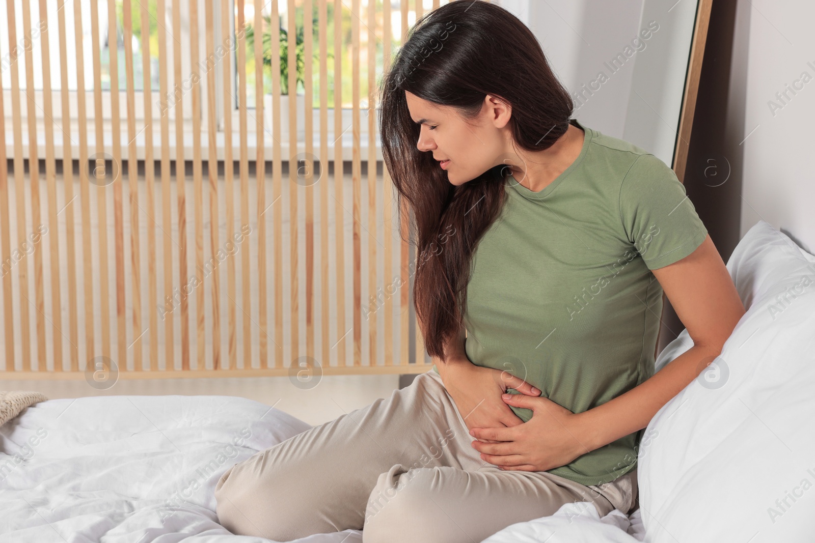 Photo of Young woman suffering from cystitis on bed at home