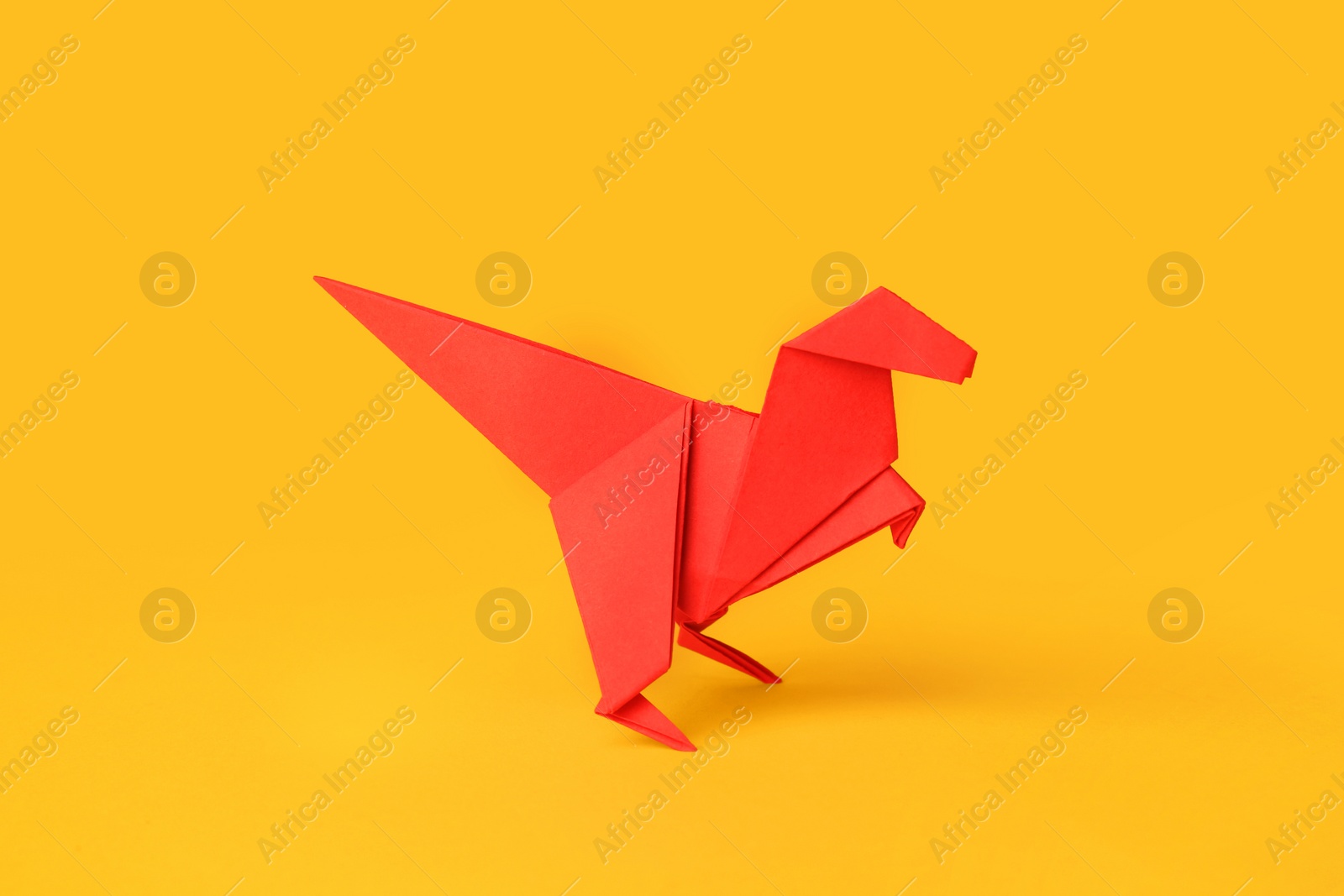 Photo of Origami art. Handmade red paper dinosaur on yellow background