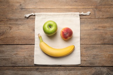 Photo of Fresh ripe apple, peach and banana with cloth bag on wooden table, top view