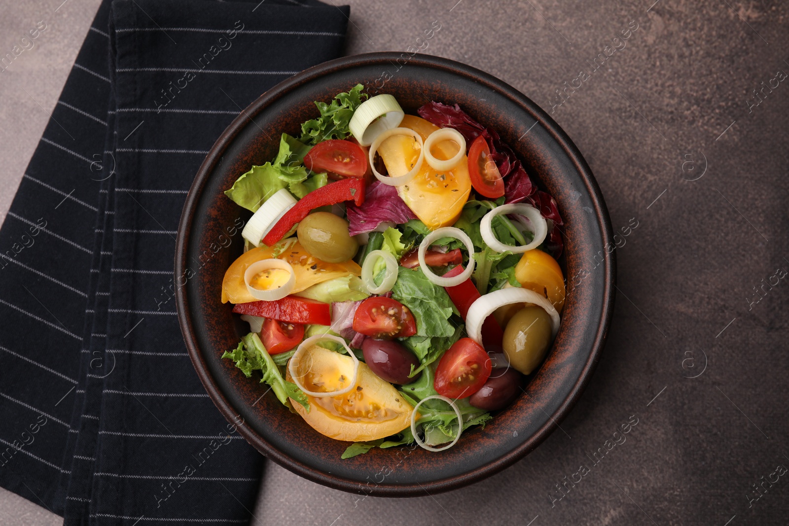 Photo of Bowl of tasty salad with leek and olives on brown table, top view