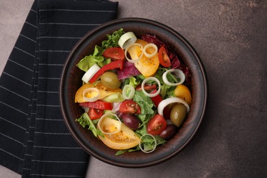 Bowl of tasty salad with leek and olives on brown table, top view