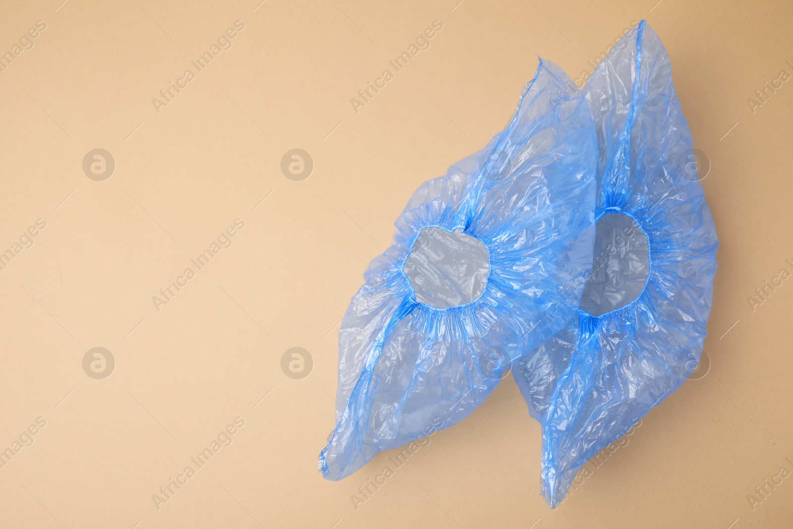 Photo of Pair of blue medical shoe covers on beige background, top view. Space for text