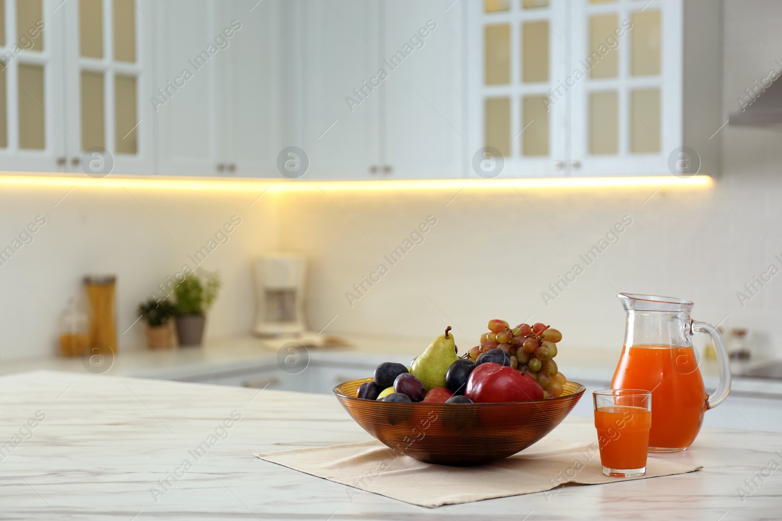 Photo of Different fresh fruits and juice on white table in modern kitchen. Space for text