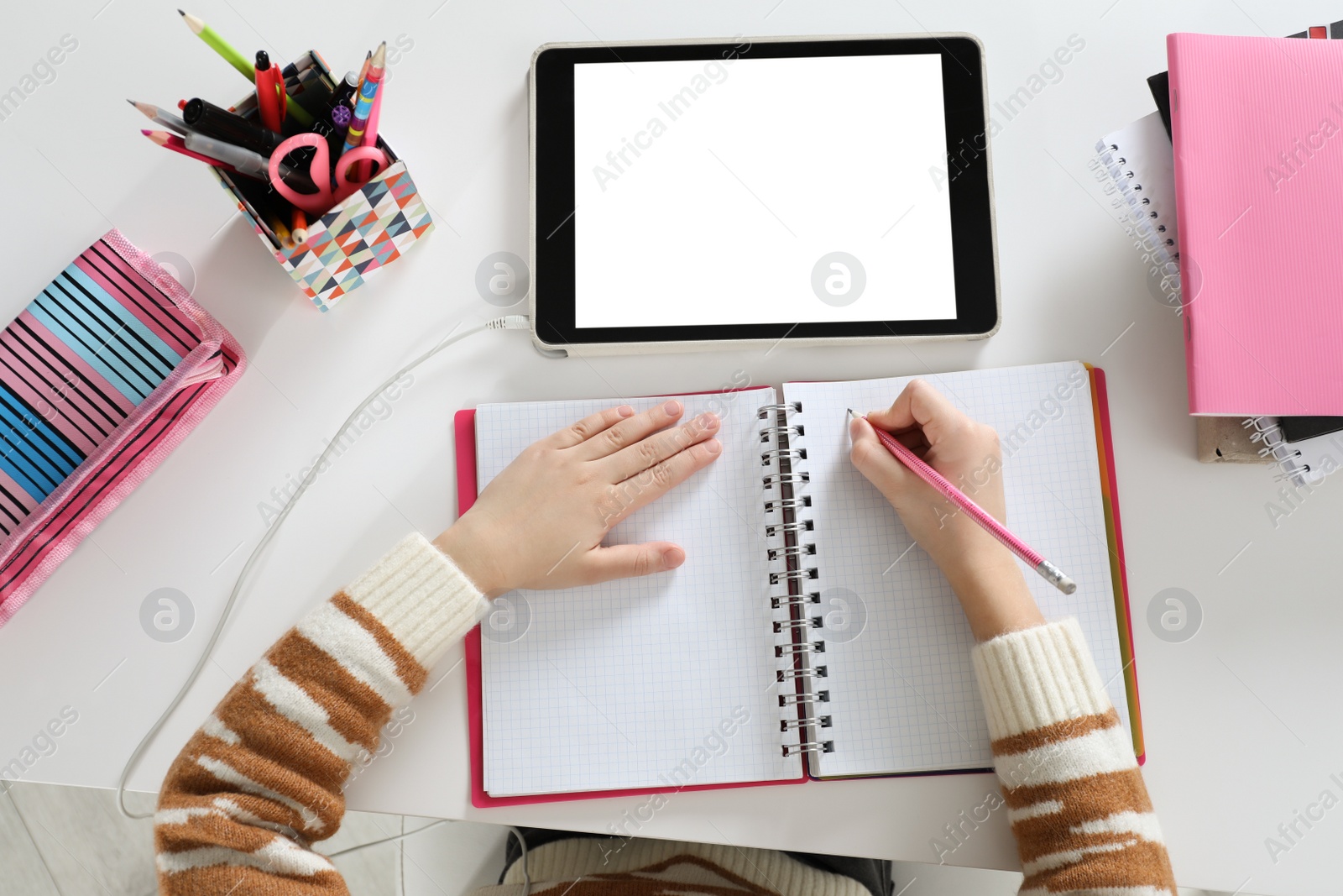 Photo of Cute little girl with modern tablet studying online at table, top view. E-learning