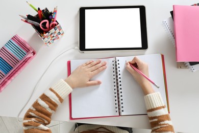 Cute little girl with modern tablet studying online at table, top view. E-learning