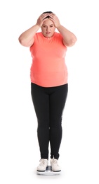 Overweight woman in sportswear using scales on white background