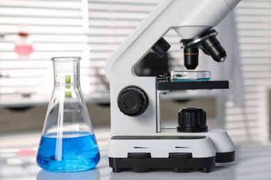 Laboratory analysis. Flask with blue liquid and microscope on white table indoors