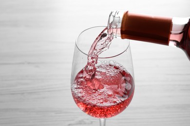 Photo of Pouring delicious rose wine into glass on white table, closeup