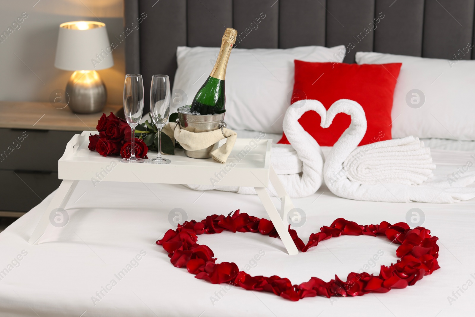 Photo of Honeymoon. Swans made with towels, heart of beautiful rose petals and sparkling wine on bed in room