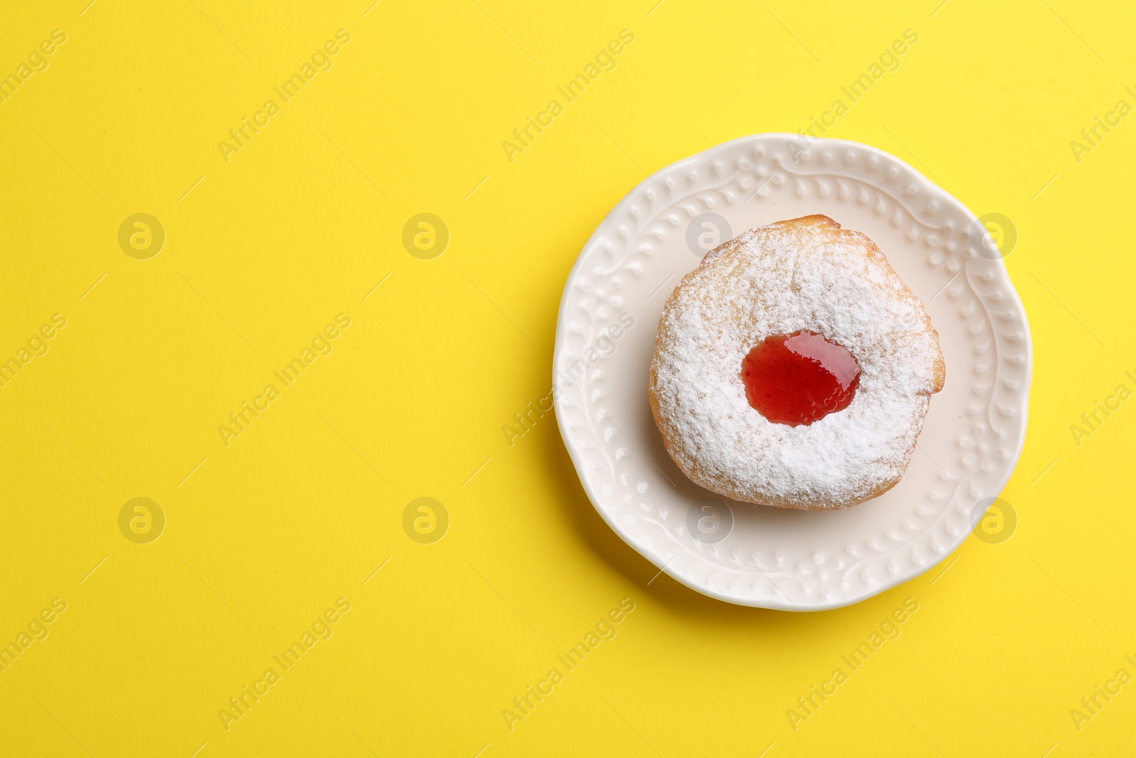 Photo of Hanukkah donut with jelly and powdered sugar on yellow background, top view. Space for text