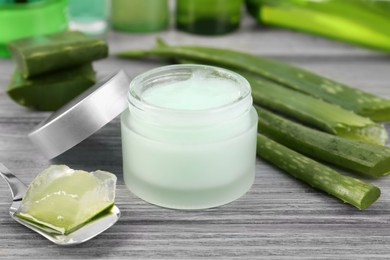 Photo of Jar with natural gel, spoon of peeled aloe vera and green leaves on light grey wooden table, closeup