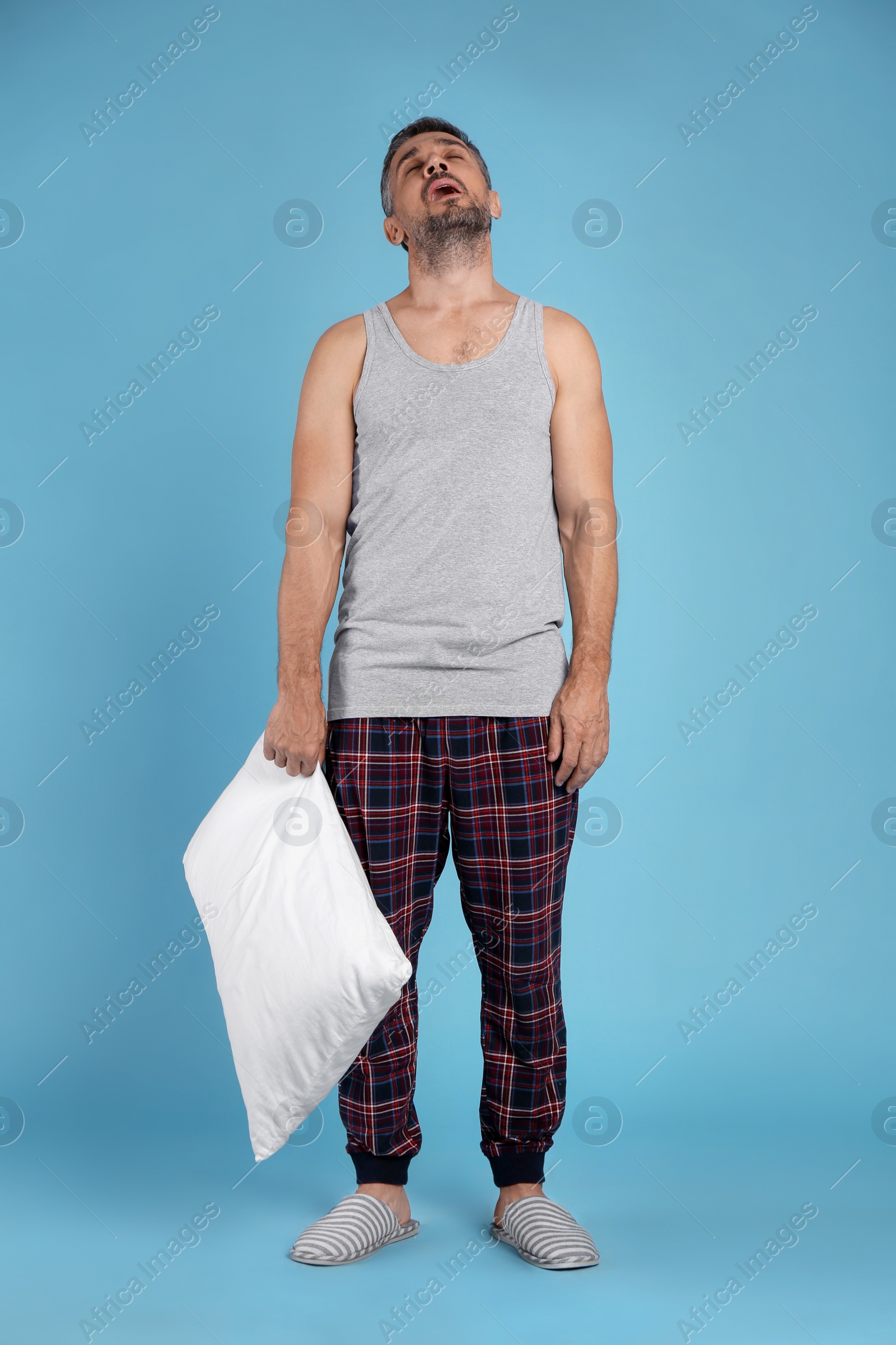 Photo of Man with pillow in sleepwalking state on light blue background