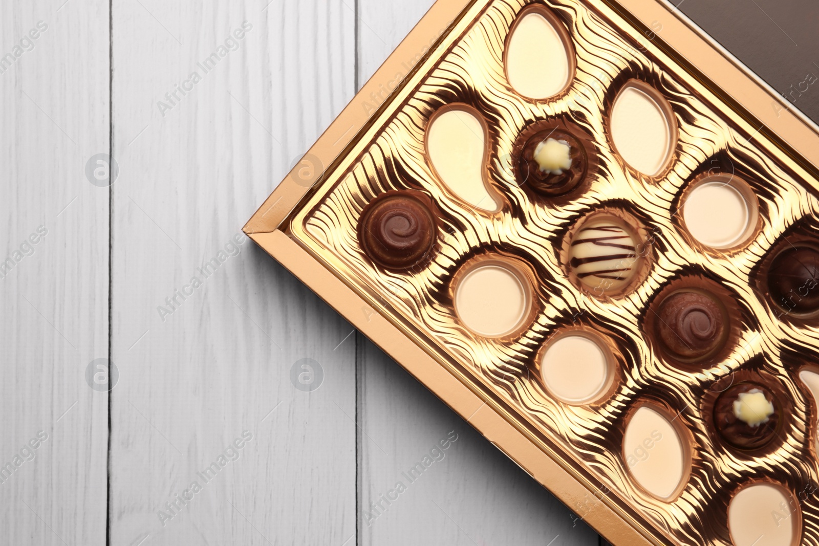 Photo of Partially empty box of chocolate candies on white wooden table, top view. Space for text