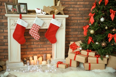 Photo of Beautiful Christmas tree and gifts near decorative fireplace with stockings indoors