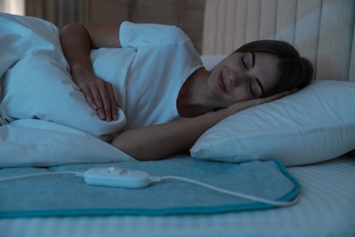 Photo of Young woman sleeping on electric heating pad in bed at night