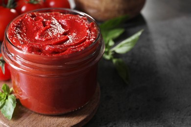 Jar of tasty tomato paste and ingredients on grey textured table, closeup. Space for text