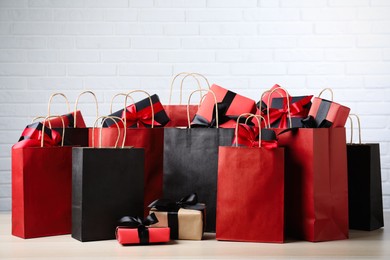 Photo of Paper shopping bags and gift boxes on table near white brick wall. Black Friday sale
