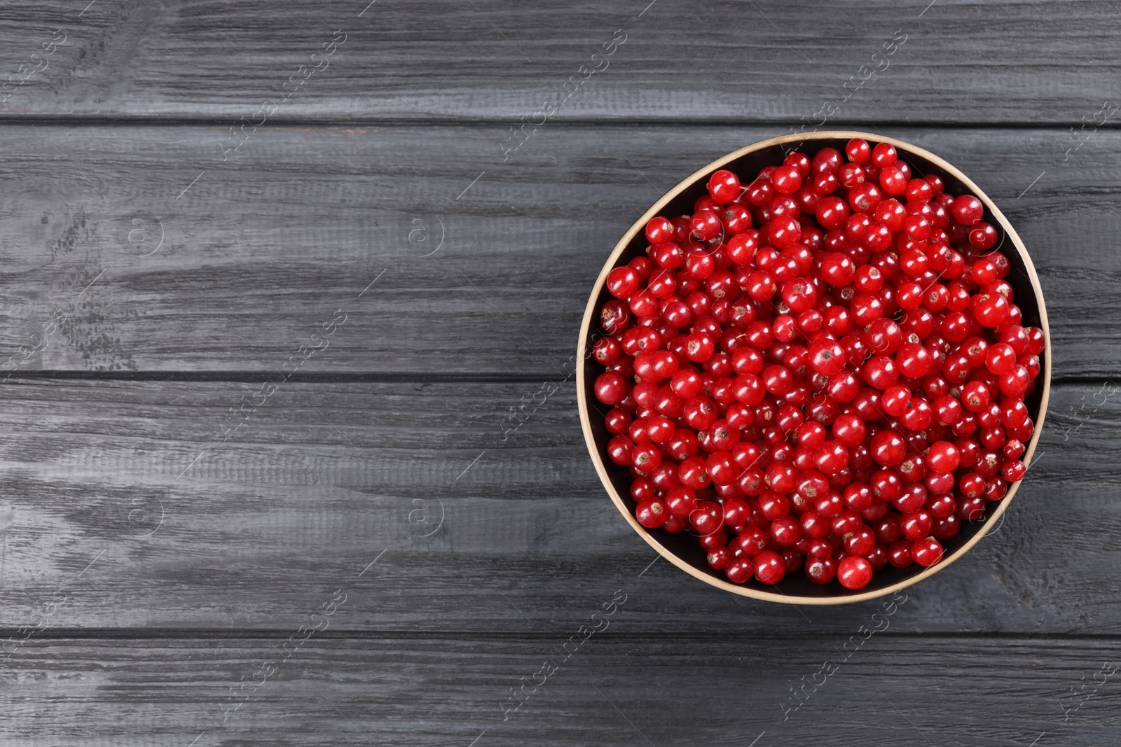 Photo of Ripe red currants in bowl on wooden rustic table, top view. Space for text