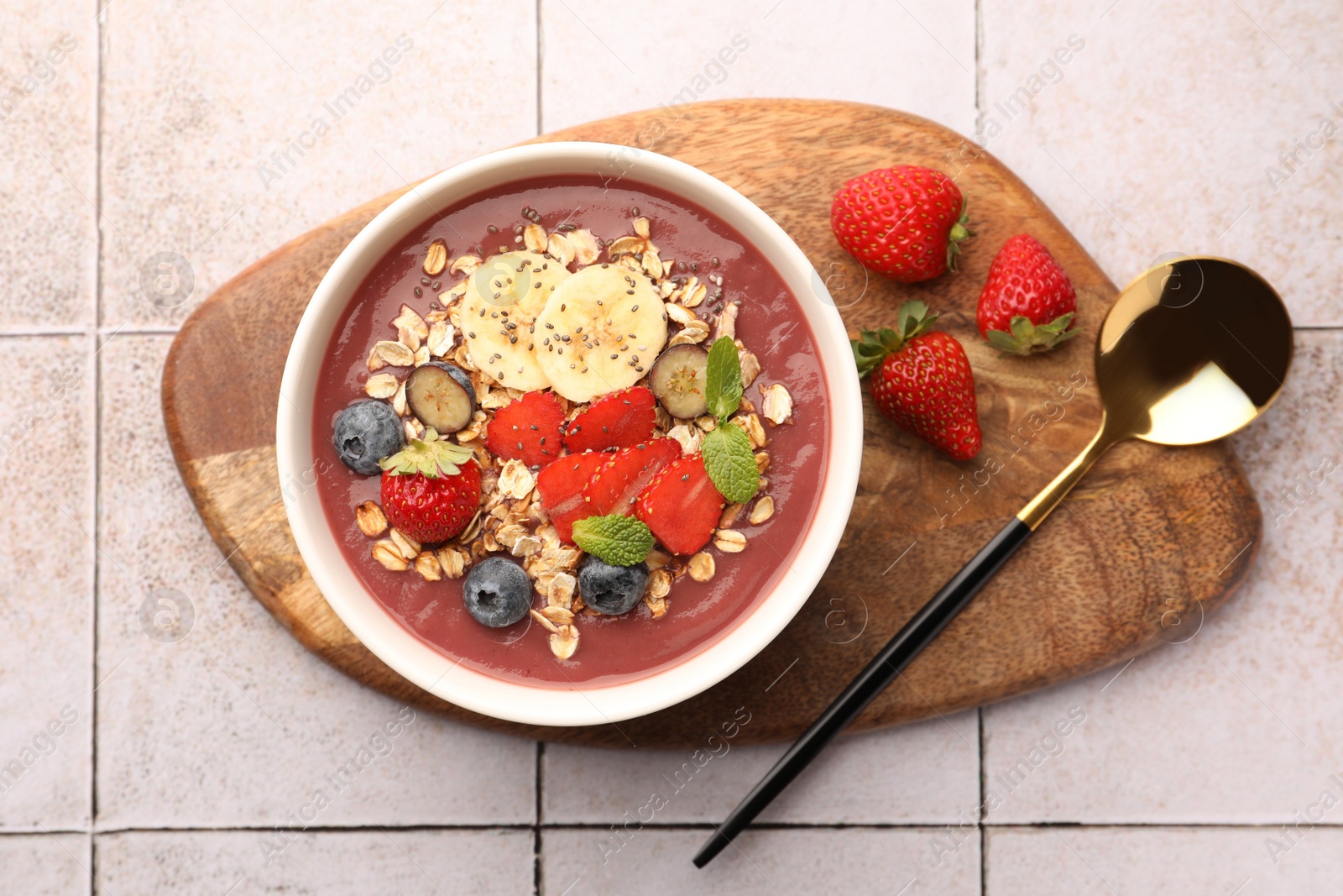 Photo of Delicious smoothie bowl with fresh berries, banana and granola on tiled surface, flat lay