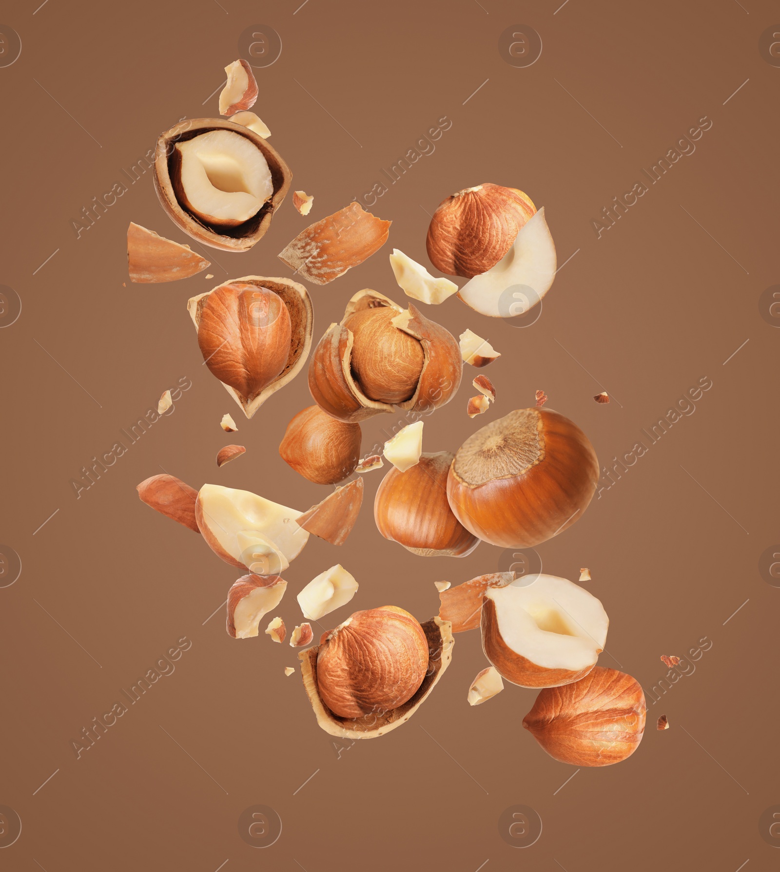 Image of Pieces of tasty hazelnuts falling on brown background