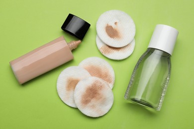 Photo of Dirty cotton pads after removing makeup and cosmetic products on green background, flat lay