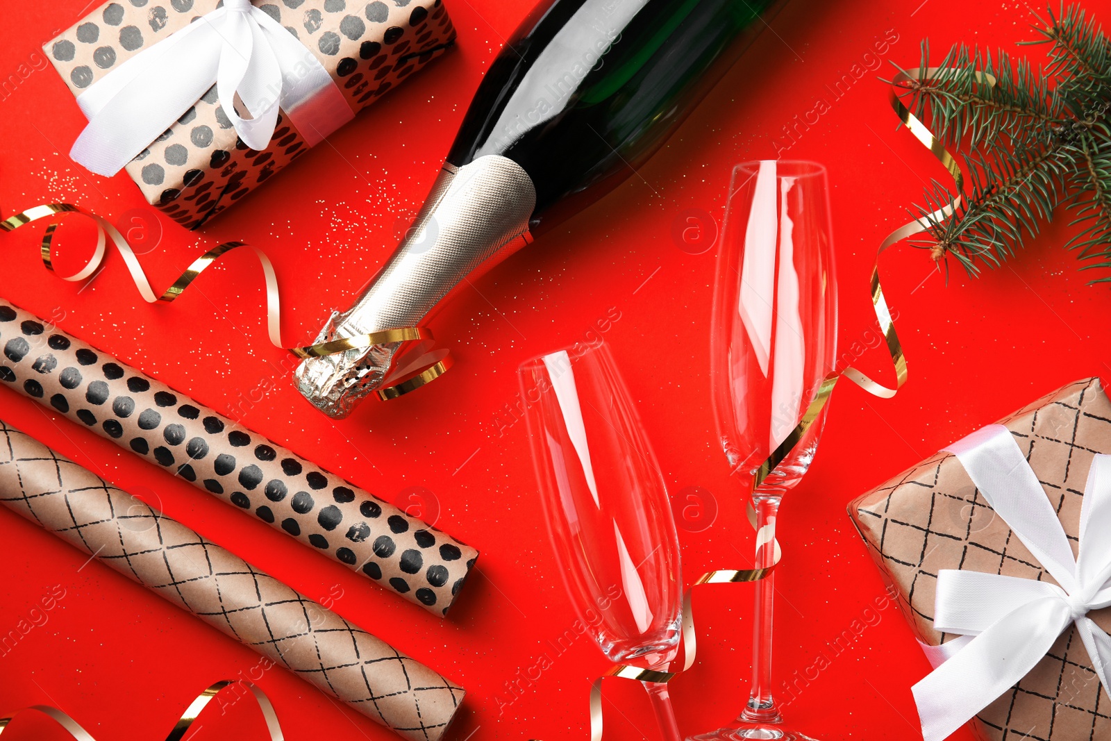 Photo of Christmas composition with bottle of champagne and glasses on red background, top view