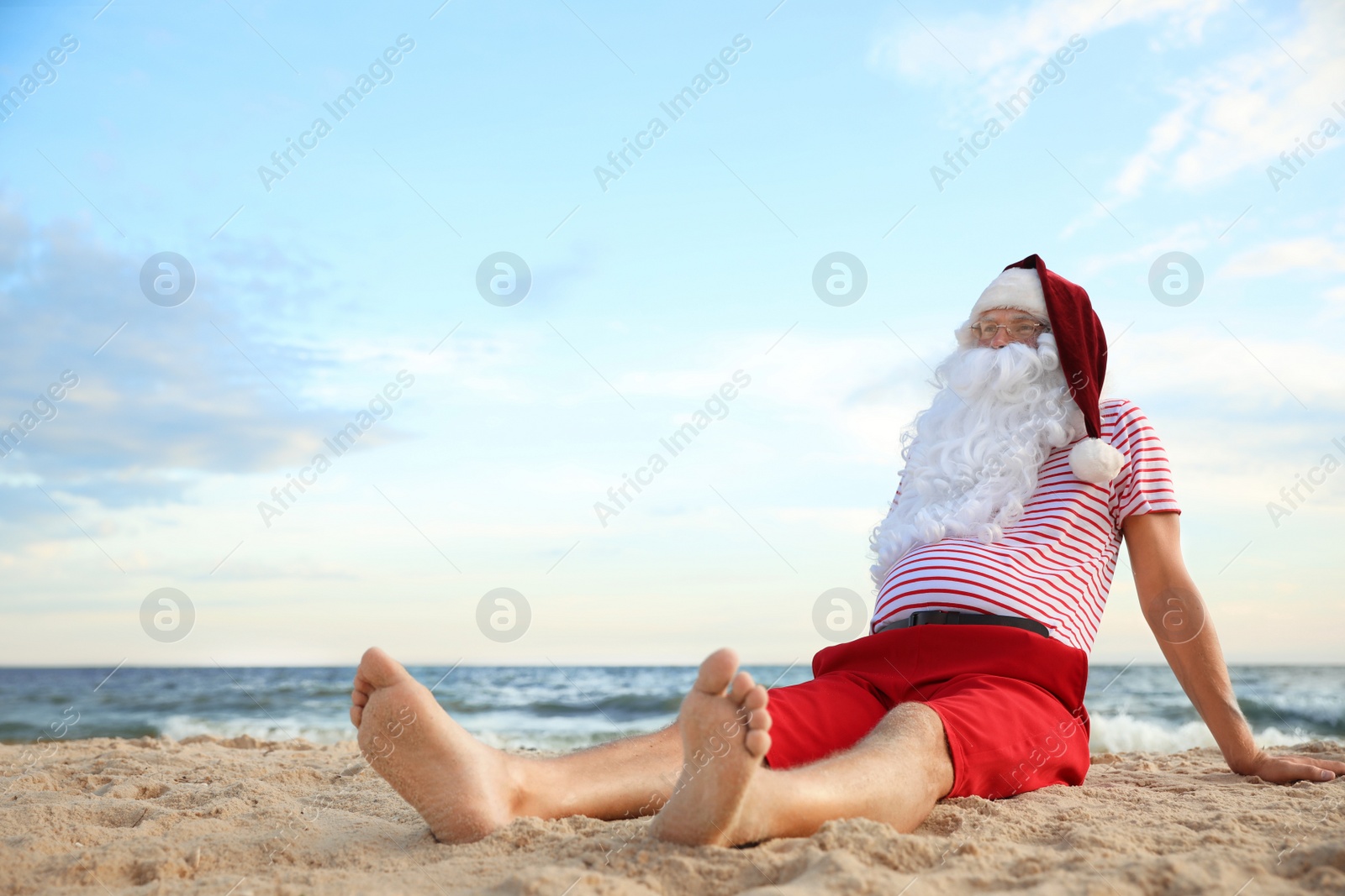 Photo of Santa Claus relaxing on beach, space for text. Christmas vacation