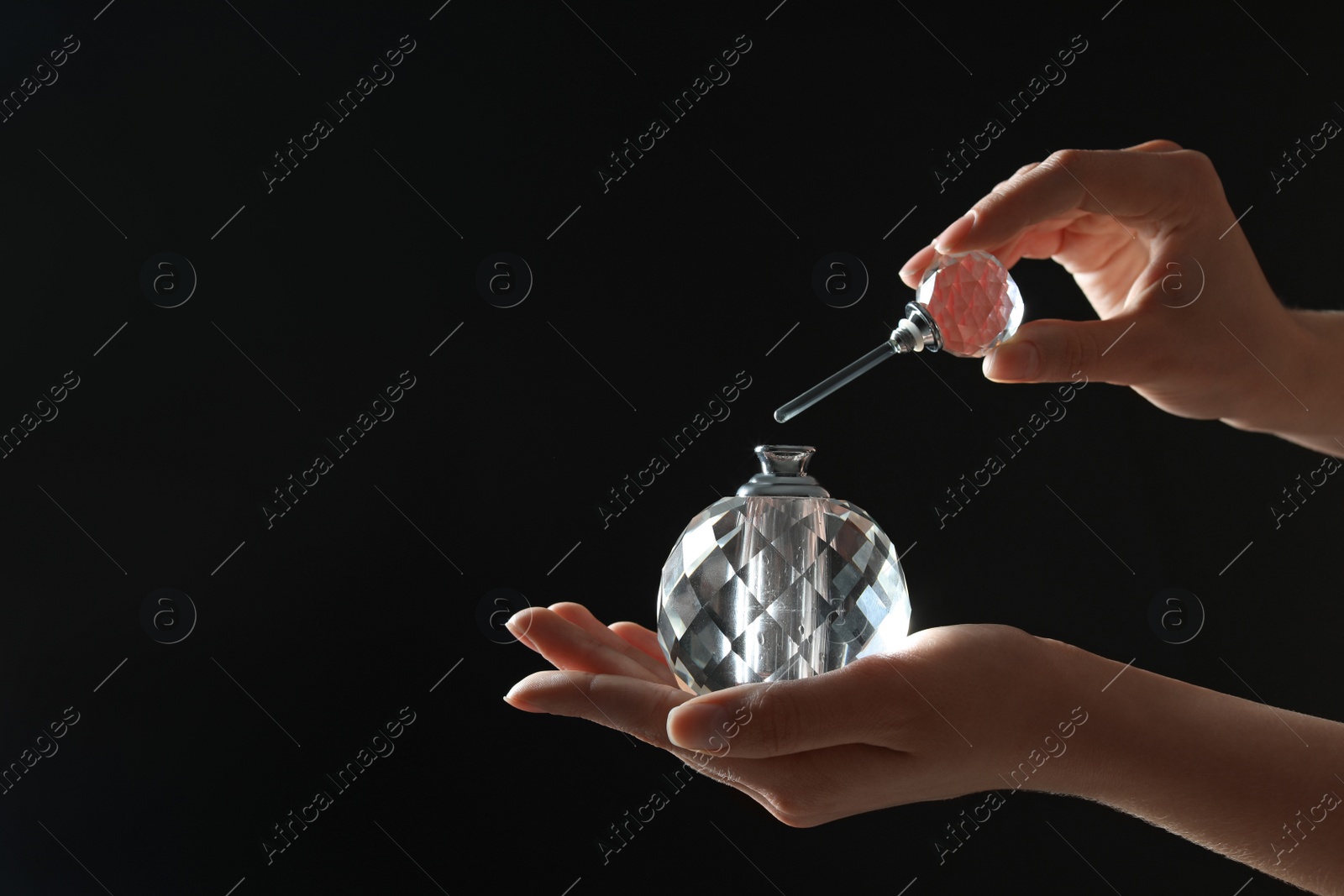 Photo of Woman holding bottle of luxury perfume on black background, closeup. Space for text