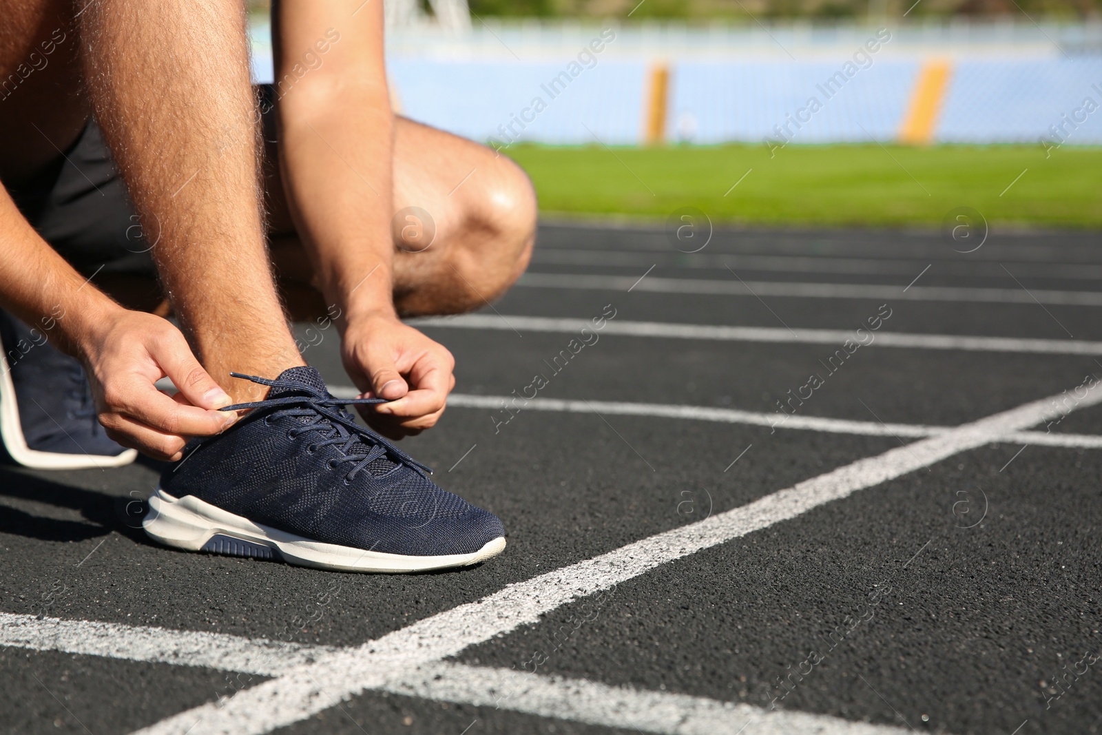 Photo of Sporty man tying shoelaces before running at stadium on sunny morning