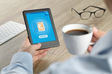 Image of Man with cup of coffee using e-book reader at wooden table, closeup