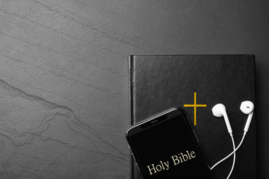 Photo of Bible, phone and earphones on black background, top view with space for text. Religious audiobook