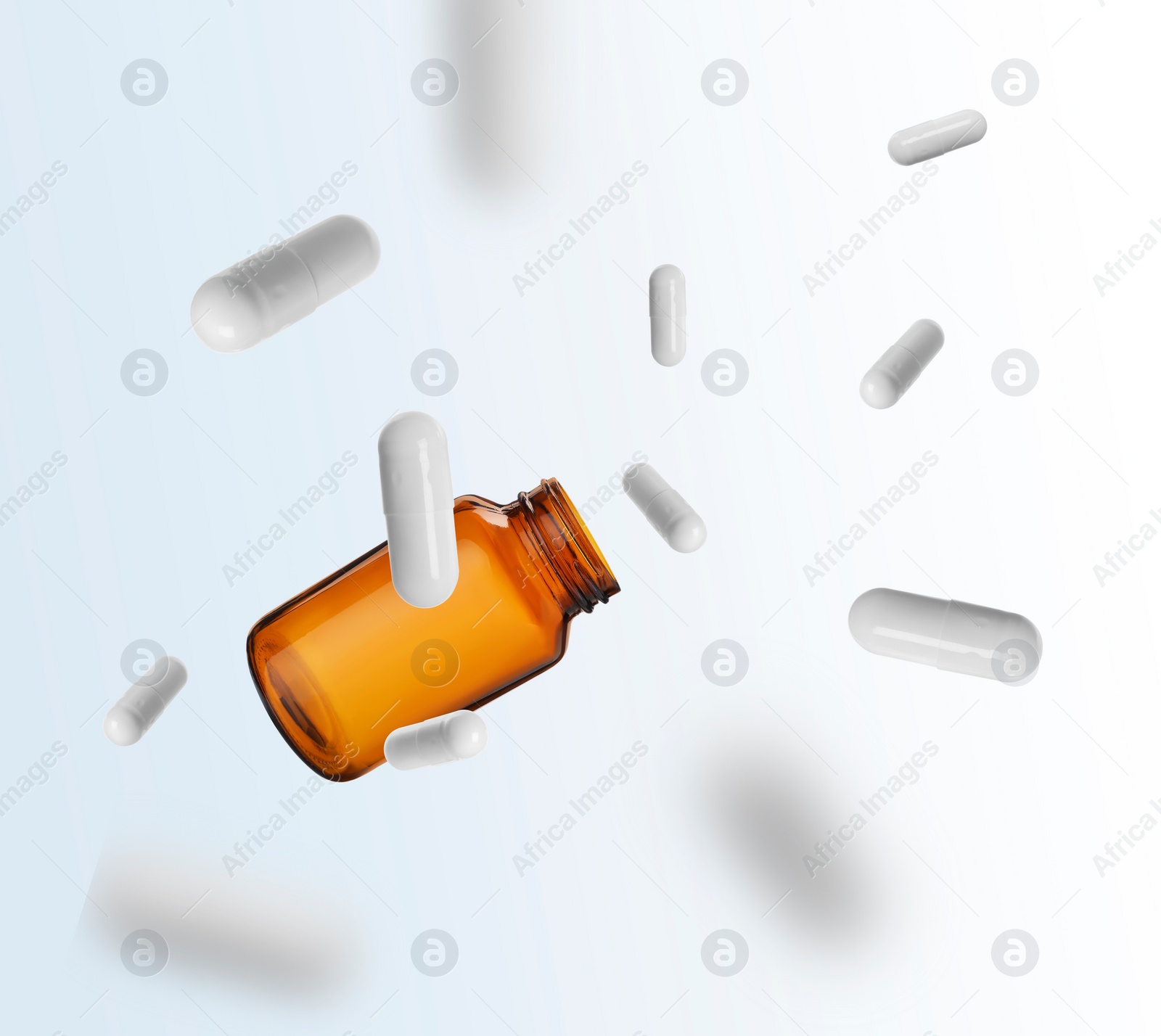 Image of Vitamin capsules and bottle in air against white background