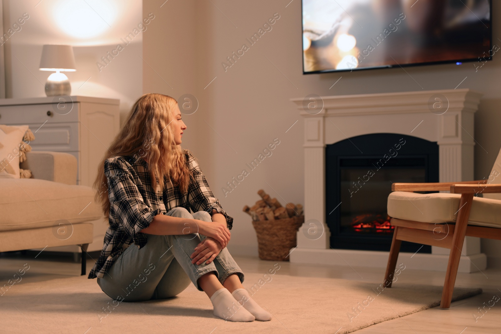 Photo of Beautiful young woman resting near fireplace at home