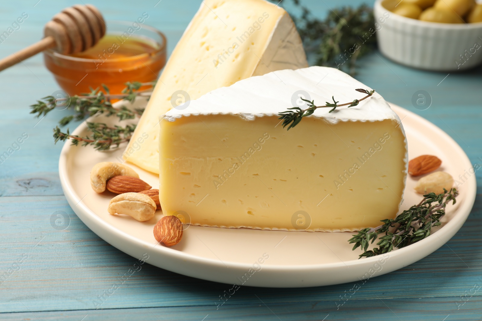 Photo of Tasty Camembert cheese with thyme and nuts on light blue wooden table