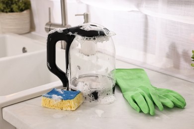 Cleaning electric kettle. Rubber gloves and sponge with foam on countertop in kitchen