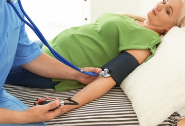 Photo of Male medical assistant measuring female patient blood pressure during home visit