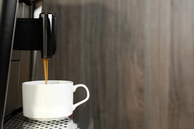 Photo of Modern espresso machine pouring coffee into cup on wooden background, closeup. Space for text