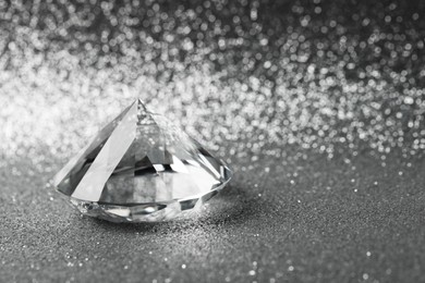 Photo of Beautiful dazzling diamond on shiny glitter background, space for text. Precious gemstone