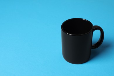 Photo of One black ceramic mug on light blue background, space for text