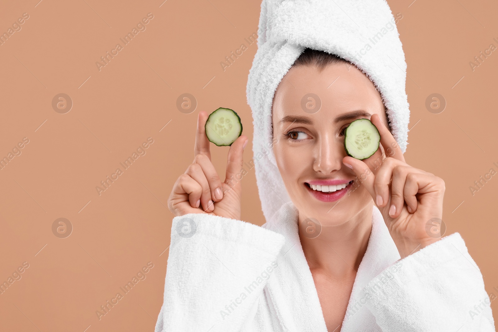 Photo of Beautiful woman covering eye with piece of cucumber on beige background, space for text
