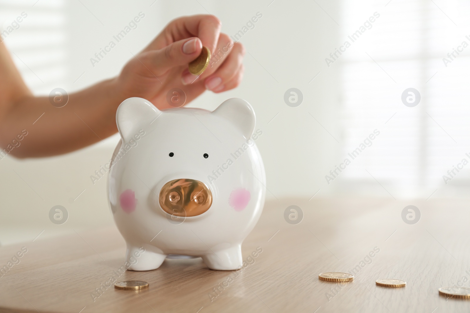 Photo of Woman putting money into piggy bank at wooden table indoors, closeup. Space for text