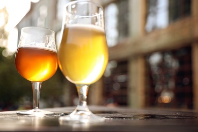 Glasses of cold tasty beer on wooden table outdoors