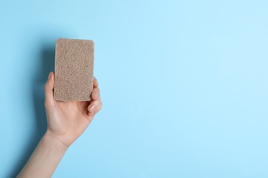 Woman holding sponge on light blue background, top view. Space for text