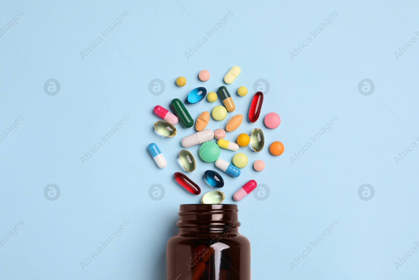 Photo of Plastic medical bottle with many different pills on light blue background, flat lay