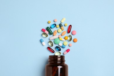 Plastic medical bottle with many different pills on light blue background, flat lay