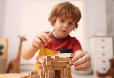 Photo of Little boy playing with wooden construction set at table in room, selective focus. Child's toy