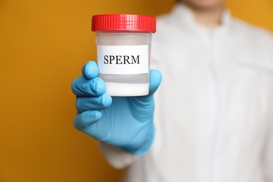 Scientist holding container with sperm on yellow background, closeup