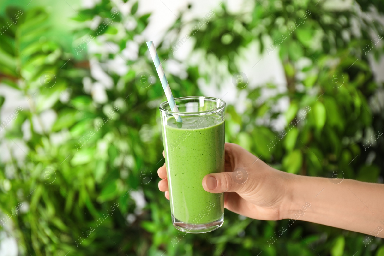 Photo of Woman holding tasty kale smoothie on blurred background, closeup