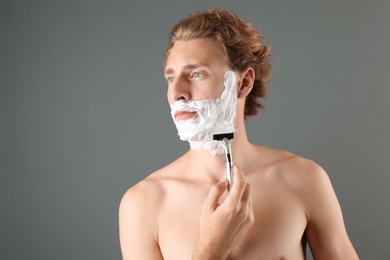 Photo of Handsome young man shaving on gray background